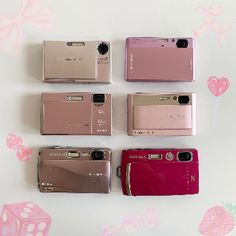 four different cameras sitting next to each other on top of a white table with pink hearts