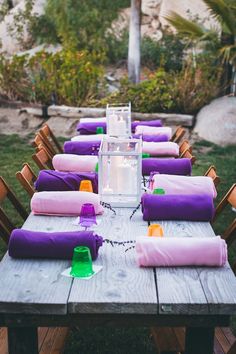 an outdoor table set up with purple and pink napkins