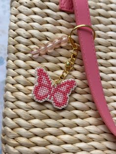 a pink butterfly keychain hanging from a woven purse on top of a wicker basket