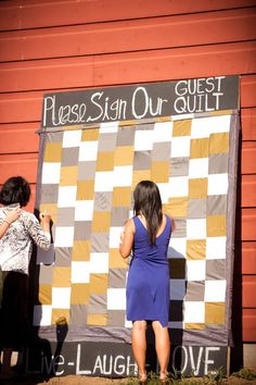 two people standing in front of a giant checkerboard sign that says please stain our quilt