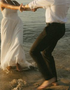 a man and woman are dancing on the beach at sunset with their feet in the water