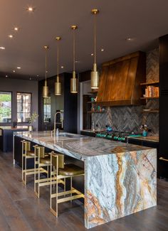 a large kitchen with marble counter tops and gold pendant lights hanging from the ceiling above it