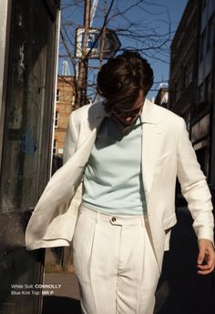 a woman is walking down the street wearing a white suit and blue shirt with her hands in her pockets