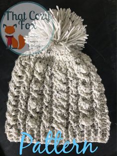 a white knitted hat with a pom - pom on top and the words that cozy fox written below it