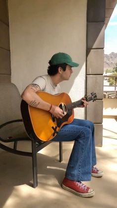 a man sitting on top of a chair holding a guitar in his hand and wearing a green hat