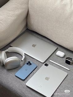 an apple laptop, headphones, and other electronics are on the couch next to each other