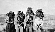 three women in long dresses are standing on a hill with large headpieces over their heads