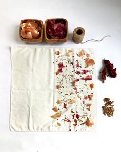 three bowls with dried fruit and herbs on top of a white table cloth next to twine spools of thread