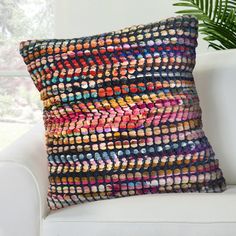 a multicolored pillow sitting on top of a white couch next to a potted plant