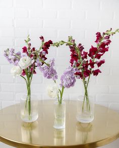 three vases with flowers are sitting on a gold table next to a white brick wall