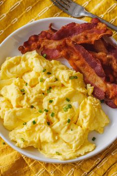 a white plate topped with eggs and bacon on top of a yellow table cloth next to a fork