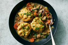 a black bowl filled with meat and vegetable stew next to a spoon on top of a table