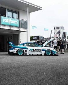 a blue and white race car parked in front of a building with people looking at it