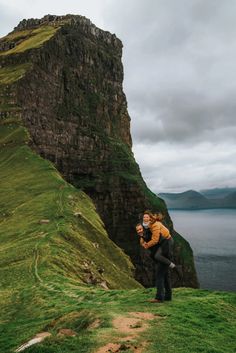 a woman standing on top of a lush green hillside next to a body of water