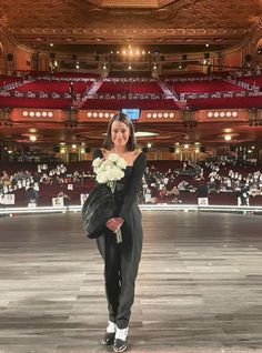 a woman standing in front of an auditorium holding a bouquet of flowers on her shoulder