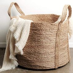 a large woven basket with tassels sits on the floor next to a white wall