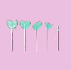 four heart shaped lollipops are lined up in a row on a pink background