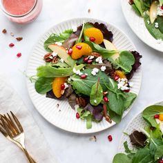 two white plates with salad on them next to silverware and a glass of orange juice