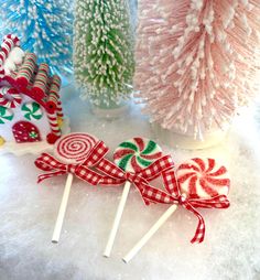 three candy lollipops are sitting in the snow next to some christmas trees