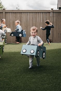 a little boy is holding a cardboard car in front of other children on the grass