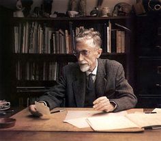 an old man sitting at a desk in front of a book shelf