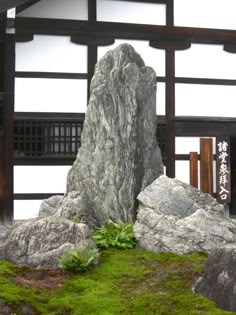 a large rock sitting in front of a building with moss growing on it's sides