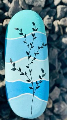 a painted rock with a plant on it in front of some rocks and water behind it