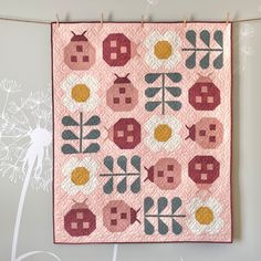 a pink quilt hanging on a clothes line with dandelions and flowers in the background