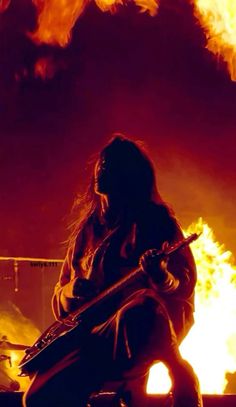 a woman sitting in front of a fire with a guitar on her lap and flames behind her