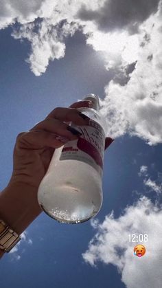 a person is holding up a bottle in the air with clouds behind them and blue sky above