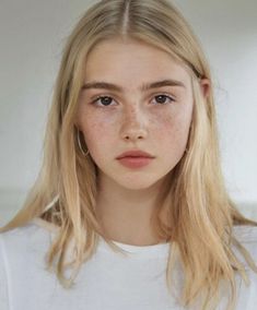 a young woman with freckles on her face looking at the camera while wearing a white t - shirt