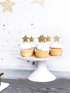 three cupcakes with white frosting and gold stars are on a cake plate