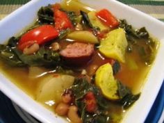 a white bowl filled with soup and vegetables on top of a blue table cloth next to a fork