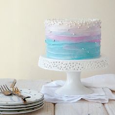 there is a cake with blue, pink and white frosting on it next to plates