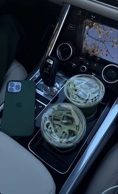 the interior of a car with two cups and an iphone on it, next to some drinks