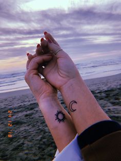 two people holding hands with tattoos on their wrists and the ocean in the back ground