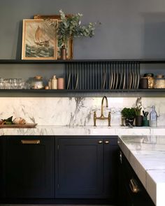 a kitchen with black cabinets and marble counter tops, gold faucets and brass pulls