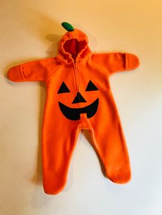 an orange baby's halloween outfit hanging on a wall with a pumpkin face drawn on it