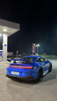 a blue sports car parked in front of a gas station at night with its lights on