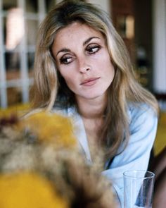 a woman sitting at a table with a glass in her hand and looking into the camera