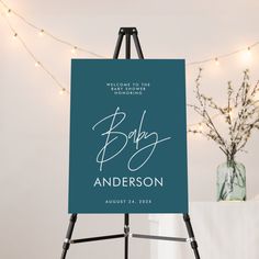 a black and white baby announcement sign on an easel with lights in the background