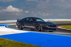 a gray sports car driving on a race track with grass and blue markings around it