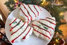 four decorated cookies sitting on top of a white plate next to a christmas tree with red and green sprinkles