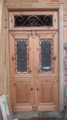 two wooden doors with wrought iron designs on the side of a brick building in front of a green chair