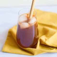 a glass filled with liquid and ice on top of a yellow cloth next to a wooden spoon