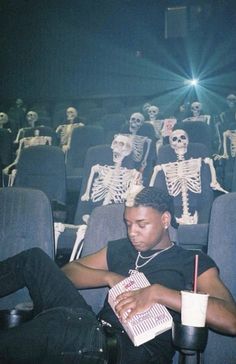 a man sitting in front of a movie theater with skeletons on the wall behind him