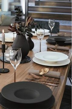 the table is set with black and white plates, silverware, and wine glasses