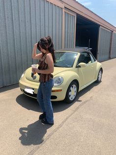 a woman standing next to a yellow car in front of a metal building with an open door