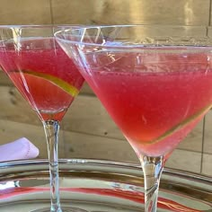 two wine glasses filled with pink liquid and lemon wedges sitting on a silver tray