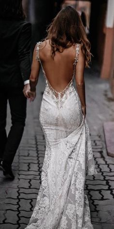 a woman in a wedding dress walking down the street with her back to the camera